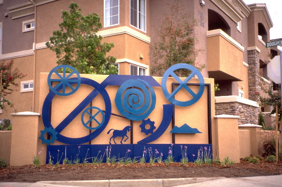 metal cutout sculptures in shades of blue, including spirals, a horse, a mountain and machinery